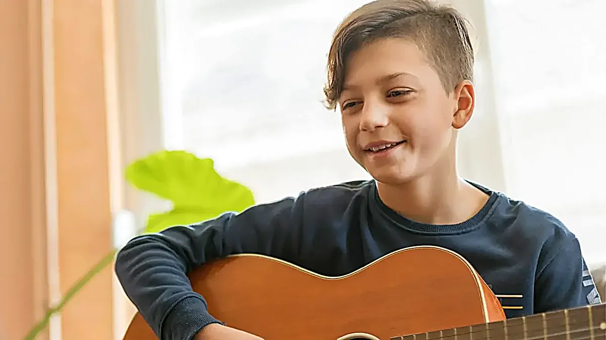 A young student smiling while playing guitar at Morningside School of Music