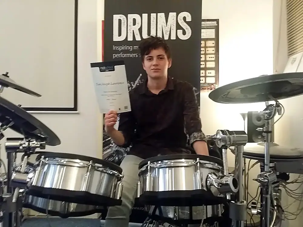 A drum student at Morningside School of Music holding his Rockschool exam certificate